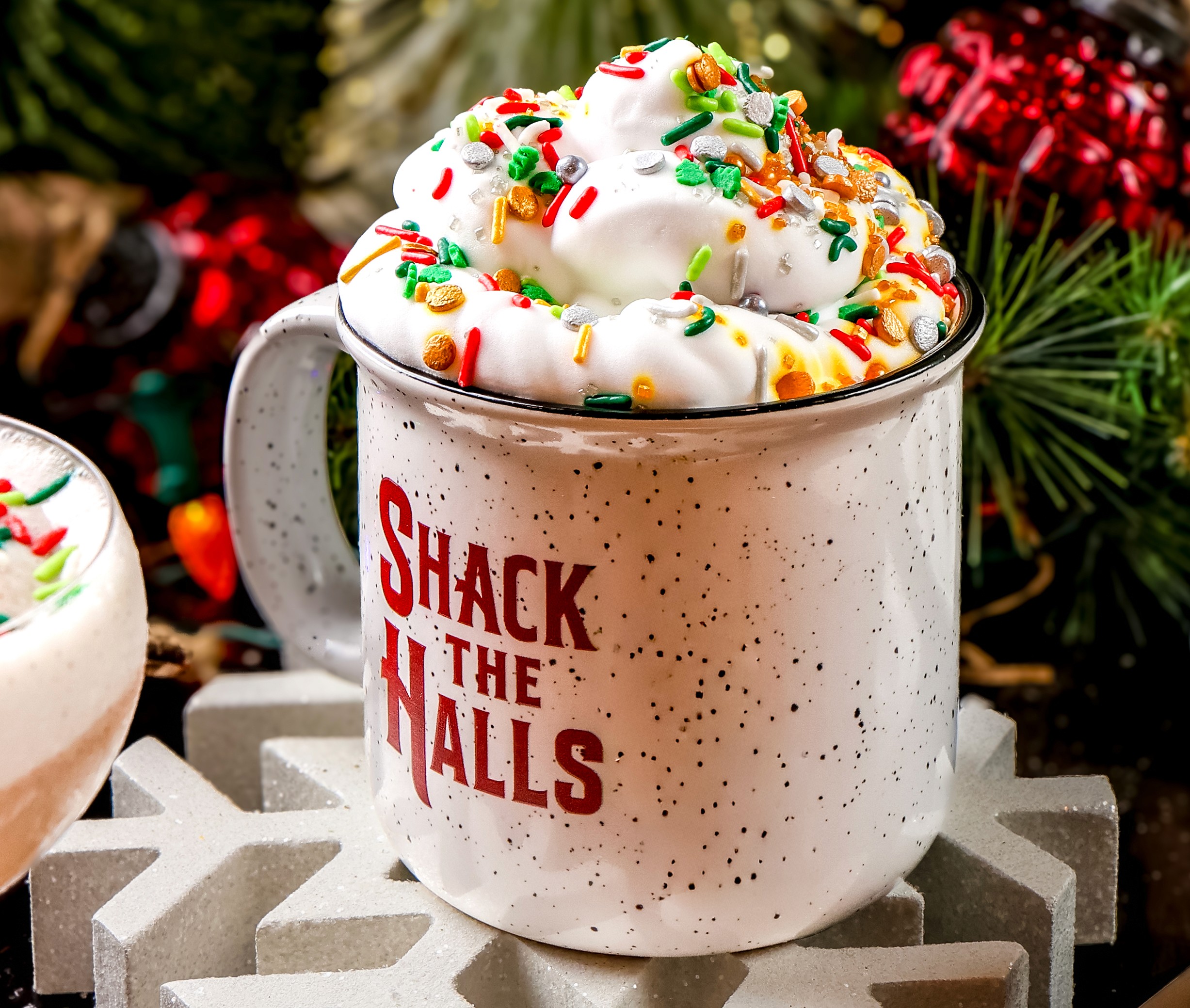 Shack the Halls branded campfire mug topped with whipped cream and holiday sprinkles